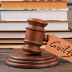 A wooden gavel with a tag reading 'Guilty' next to stacked books