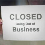 A person holding a sign that reads 'CLOSED Going Out of Business'