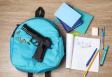 Kid Shoots Teacher – Then Himself! A blue backpack with a handgun and school supplies on a wooden surface