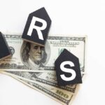 Blocks spelling 'IRS' placed on top of hundred dollar bills featuring Benjamin Franklin