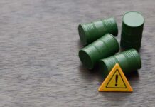 Four green barrels and a warning sign on a wooden surface