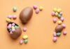 Chocolate Easter eggs and colorful candy eggs on an orange background