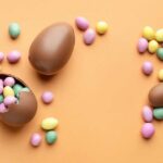 Chocolate Easter eggs and colorful candy eggs on an orange background
