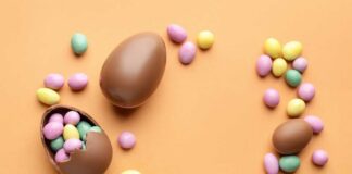Chocolate Easter eggs and colorful candy eggs on an orange background
