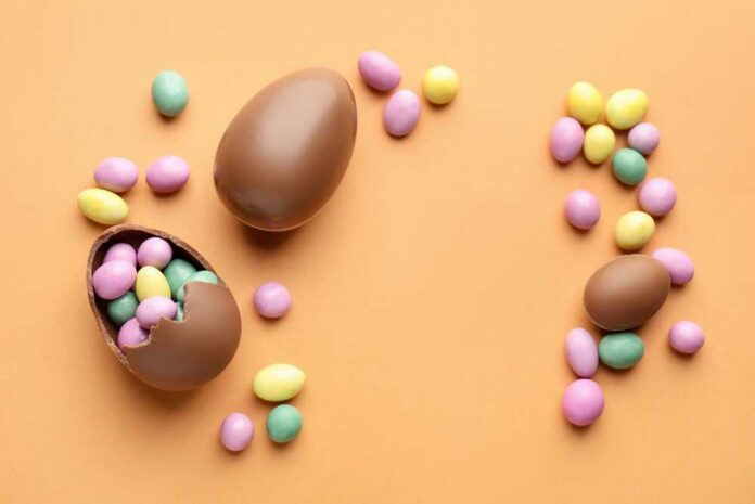 Chocolate Easter eggs and colorful candy eggs on an orange background