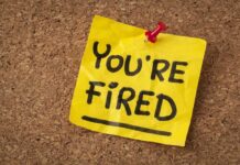 A yellow sticky note pinned to a corkboard with the words 'YOU'RE FIRED' written on it