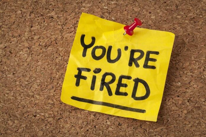 A yellow sticky note pinned to a corkboard with the words 'YOU'RE FIRED' written on it