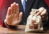 Businessman holding a money bag with a raised hand signaling refusal