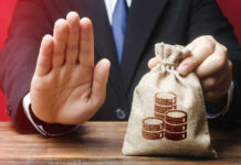 Businessman holding a money bag with a raised hand signaling refusal