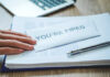 A hand resting on an envelope labeled 'YOU'RE FIRED' on a desk with papers and a pen