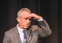Robert F Kennedy in gray suit shielding eyes.