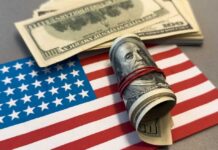 A roll of hundred dollar bills placed on an American flag