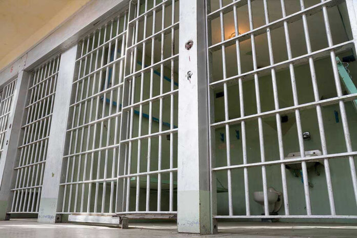 Empty prison cell with metal bars and toilet.