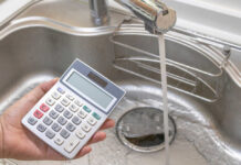 A hand holding a calculator above a kitchen sink with running water