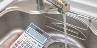A hand holding a calculator above a kitchen sink with running water