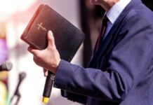 Man holding a Bible during a speech or presentation.