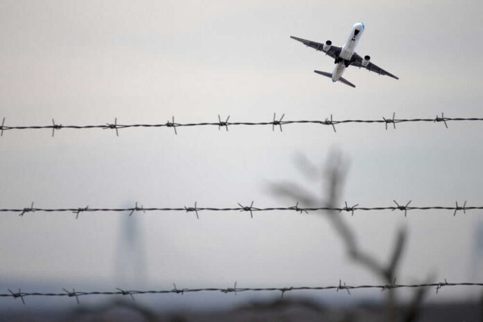 Airplane taking off view through barbed wire fence