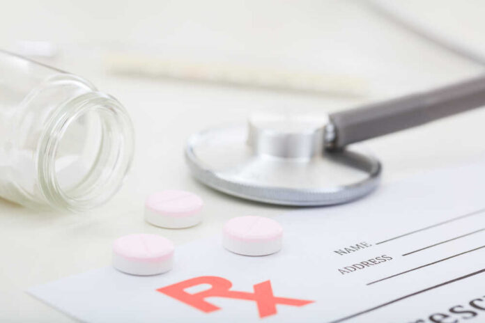 Pills,Out,Of,A,Bottle,On,White,Background A stethoscope, prescription pad, and pink tablets on a table
