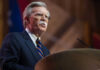 Bolton’s Shocking Flip: Guilty, But Why So Light? Man speaking at a podium with microphone.