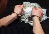 Person in handcuffs surrounded by cash