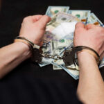 Person in handcuffs surrounded by cash