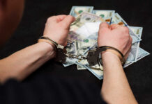 Person in handcuffs surrounded by cash