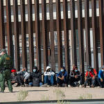 Border Bombshell: Trump Scores Supreme Win Border patrol officer watches group sitting by a fence.