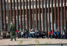 Border Bombshell: Trump Scores Supreme Win Border patrol officer watches group sitting by a fence.