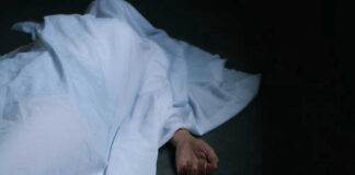 Hand emerging from under white sheet on dark surface.