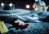 Crime scene with covered body and hand exposed.