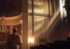 A clergy member standing in a church with light streaming through windows