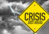 Wall Street Villain, Real Problem Ignored? Yellow sign reading Crisis Just Ahead with stormy sky