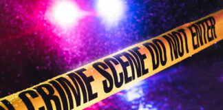 Crime scene tape with flashing lights in background.