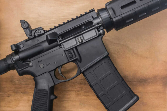shutterstock_1886906086 Black rifle on wooden surface close up