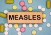Measles Explosion Stuns America Wooden block with the word 'MEASLES' surrounded by various pills