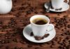 A white coffee cup filled with coffee on a wooden table surrounded by coffee beans