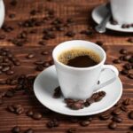 Coffee Shock: Heart Risk Drops Why? A white coffee cup filled with coffee on a wooden table surrounded by coffee beans