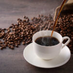 Botulism Warning Hits THIS Coffee? Cup of hot coffee being poured beside scattered coffee beans