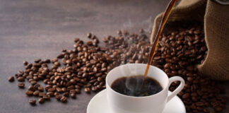 Cup of hot coffee being poured beside scattered coffee beans