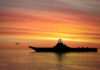 Warship Blackout Stuns Navy Families Silhouette of an aircraft carrier at sunset.