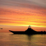 Warship Blackout Stuns Navy Families Silhouette of an aircraft carrier at sunset.