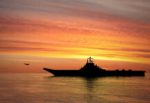 Warship Blackout Stuns Navy Families Silhouette of an aircraft carrier at sunset.