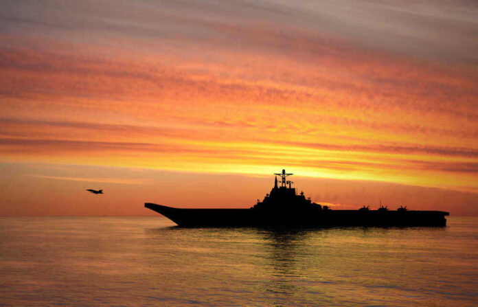 shutterstock_1449359894 Silhouette of an aircraft carrier at sunset.