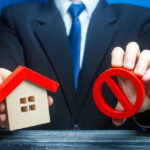 Businessman holding house model and prohibition sign