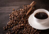 A cup of hot coffee next to spilled coffee beans and a wooden scoop