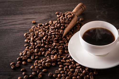 Coffee,Beans,And,Hot,Coffee,On,The,Table A cup of hot coffee next to spilled coffee beans and a wooden scoop