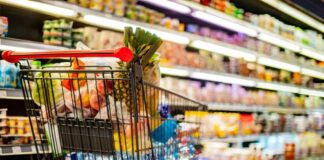 Shopping cart filled with various groceries in a supermarket aisle