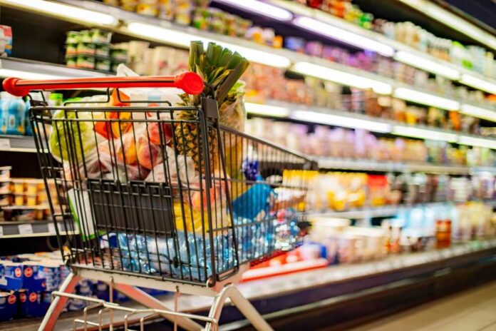 A,Shopping,Cart,With,Grocery,Products,In,A,Supermarket Shopping cart filled with various groceries in a supermarket aisle