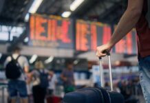 Airport Foot-Wash Fight Erupts A traveler holding a suitcase in an airport terminal with a flight information display in the background