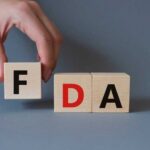 A hand holding a wooden block with the letter F, next to blocks spelling FDA